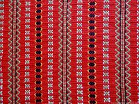 Close-up of the table runner showing a red base color woven with stripes of small white motifs, black dots, and wavy beige lines.