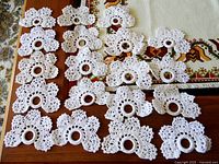 19 white crocheted serviette holders laid out in rows on a wooden surface showing their overall design and quantity.