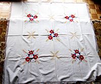 Full view of the large square white cotton tablecloth with multicolored floral and wheat hand embroidery and crocheted edge.