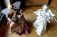 Wide view of both angel figurines side by side on a wooden floor next to a window.