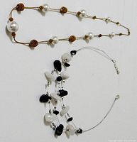 Photo of two necklaces laid flat; one with faux pearls and wooden beads on brown cord, the other multi-strand with black and white beads on wire.