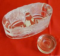 Two glass candle holders on a red background, large holder with a chip repaired and floral etching, smaller plain cylindrical holder