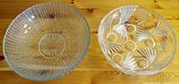 Top view of two large clear glass bowls, one with ribbed cut glass pattern, the other with etched circular and leaf designs.