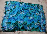 Full view of the large blue floral batik scarf with fringed edges showing overall pattern and colors