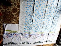 Photo showing the two large tablecloths spread on the floor, one with a blue floral print and the other winter snowman scene, providing a size and pattern overview.
