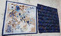 Pair of two square scarves laid flat showing one floral patterned scarf and one dark blue abstract pattern scarf.