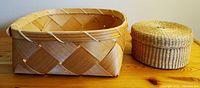 Photo showing a square woven basket and a round woven basket with lid on a wooden surface.