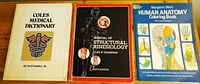 Three medical and anatomy books on a wooden table: Coles Medical Dictionary, Manual of Structural Kinesiology, Human Anatomy Colouring Book.