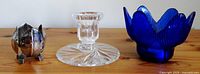 Three candle holders on wooden surface: metal on left, clear glass in center, blue glass on right
