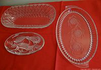 Three clear glass dishes displayed on a red cloth: small oval bell design, deep rectangular diamond cut, and oval etched floral dishes.