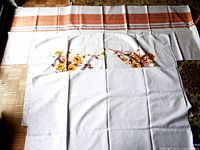 Three tablecloths stacked, showing floral detail on the middle cloth and parts of the striped cloth.