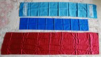 Three scarves laid flat on a light surface showing full length and color: turquoise, blue, and red.