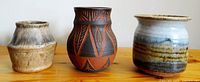 Three pottery vases on a wooden surface, front view showing varied shapes and designs