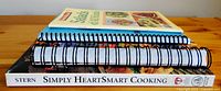 Four cookbooks stacked horizontally showing titles and spines, mostly spiral-bound except one book.