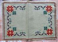 Top-down photo showing two green placemats with embroidered floral and geometric corner patterns.