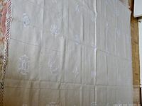 Large square beige tablecloth with white embroidered floral designs and lace edge.