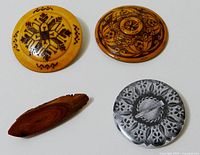 Four Estonian pins shown together: three round wood pins with burnt patterns and one metal pin, laid out on white background.