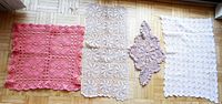 Four lace mats laid out on wooden floor showing the different colors, sizes, and shapes: dark pink square, beige rectangle, pale brown diamond, and white rectangle with minor stains.