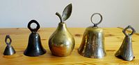 All five brass bells lined up on a wooden surface showing different sizes and shapes including the pear-shaped and 1991 inscribed bell.