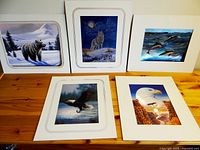 Group view of five matted metallic-look wildlife pictures including bear, wolf, porpoise, eagle, and bald eagle, shown on wood surface.