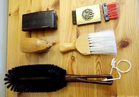 Top-down view of five various brushes arranged on wooden surface showing bristle colors and shapes, including hedgehog-shaped wooden brush and large black bristle brush with wooden handle.