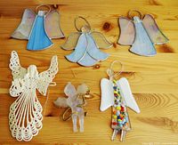 Six angel decorations displayed on a wooden surface: four stained glass, one plastic with beads, one starched yarn angel.