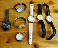 Top-down image showing all seven vintage watches arranged on a wooden surface with various straps and dial designs.