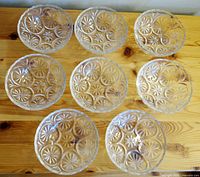 Eight clear cut glass dessert bowls laid out on wooden surface showing detailed starburst patterns and scalloped rims.