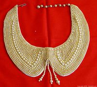 Full top-down view of golden-colored beaded collar necklace on red background showing shape and bead pattern.