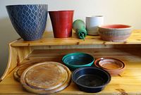 Full view of flowerpots and wooden bases on top shelf and plastic and ceramic saucers below on bottom shelf, showing size and condition