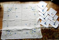 Full view of tablecloth laid flat with eight matching embroidered napkins arranged to the side