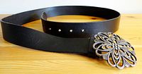 Black leather belt coiled with visible holes and the ornate floral buckle attached.