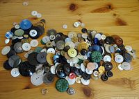 Buttons of various sizes, materials, and colors scattered on a wooden surface showing diversity of shapes and designs.
