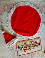 Photo showing all three items laid out on a carpet: round red felt tablecloth with white fringe, felt Santa hat, and linen table runner with two gnomes playing instruments