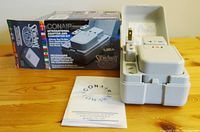 Photo showing the closed gray plastic storage case with the converter unit and three adaptor pieces inside, shown alongside the product box and instruction manual.