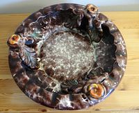 Top-down view showing the round ceramic dish with mottled interior and three raised orange flowers with leaves around the scalloped edge.