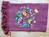 Full view of the embroidered wall hanging showing the rose-colored fabric with floral embroidery and fringe.