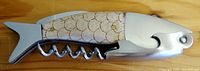 Fish-shaped bottle opener with corkscrew, wooden handle engraved with scales, and metal fish head and tail visible from top view.