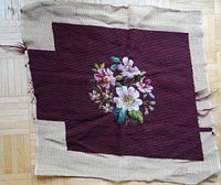 Floral needlepoint embroidery with colorful flowers and green leaves on a burgundy background with beige canvas edges.