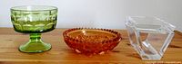 Clear glass box with lid, orange dish, and green glass bowl arranged on wooden surface