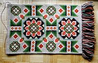 Full view of embroidered wall hanging showing entire rectangular textile piece with colorful geometric floral patterns and multicolor fringe on the right side.