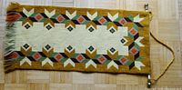 Full view of the rectangular needlepoint wall hanging laid flat, showing geometric floral border and fringe detail.
