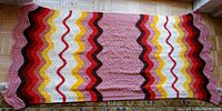 Full view of the large knitted shawl showing overall size and brightly colored zigzag pattern