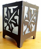 Black metal maple leaf candle holder showing three side panels with frosted glass inside. Front angled view.