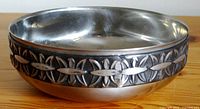 Angle view of pewter bowl showing decorative raised geometric pattern band around the outside and smooth interior