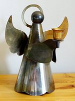 Front view of metal angel candle holder showing head, wings, and candle cup held in one arm.