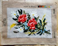 Full view of needlepoint canvas showing two red roses with various foliage and flowers, 'Made in France' text visible on fabric top edge.