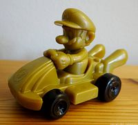 Side view of yellow plastic Mario figure in go-kart toy showing profile and detailed kart features
