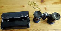 Tasco opera glasses alongside original matching black leather case with stitched edges and snap button flap