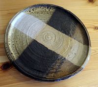 Top view of pottery plate showing four-quadrant brown, black, and beige pattern with central concentric circle design.